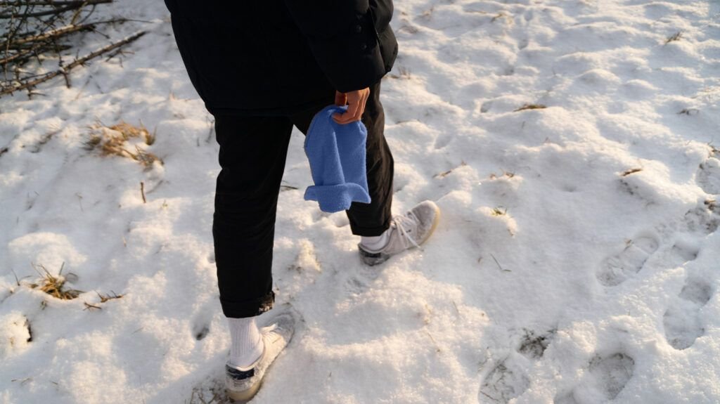 someone holding a blue beanie while walking through the snow