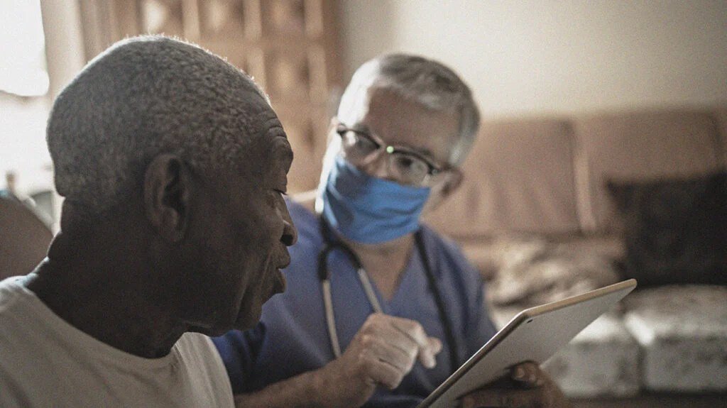 A doctor in a mask asks an older male to fill out a form