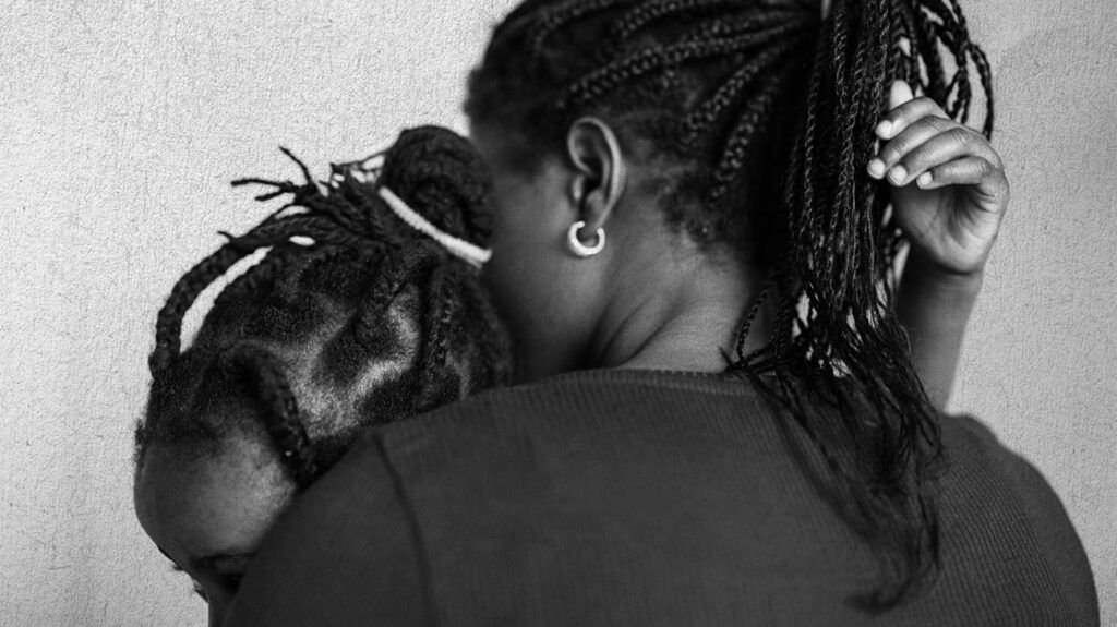 Black and white image, a mother holding a child, faces obscured.